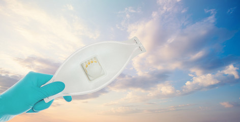 Protective madical face mask in hands in doctor gloves on sky clouds background, safety and virus...