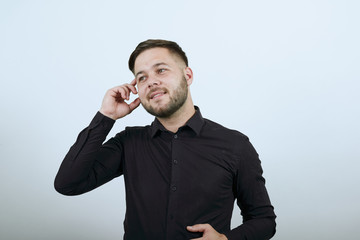 Young Bearded Dark Haired Man In Black Stylish Shirt On White Background, Dreamy Man Holds Fingers To Head, Came Up With A New Idea, Thinks With His Brain. Concept Of The Smart People