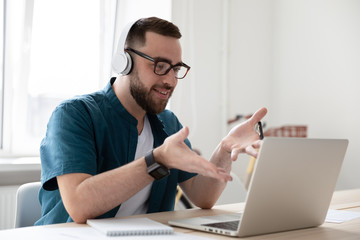 Smiling businessman in headphones looking at laptop screen watching webinar. Happy young bearded...