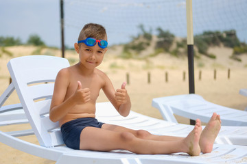 Young guy in swimming glasses is sunbathing on a sunbed on the sea beach.