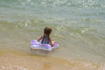 Little girl in an inflatable circle on the beach. A child bathes in the sea.