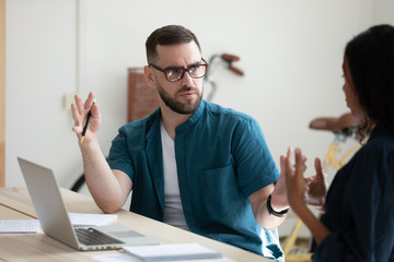 Serious businessman perplexed by female colleague decision in office at meeting. Indignant man listening business manager using laptop for presentation new project concept.