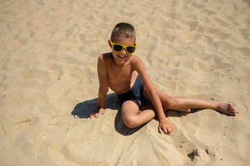 Little boy in sunglasses on the beach. Child in swimming trunks on the sea sand.