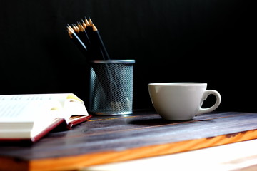 white coffee cup on wood floor with pencails in container isolate on black background