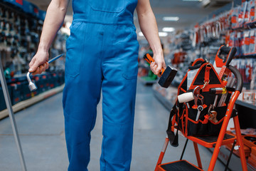 Male worker holds wrench and hammer in tool store