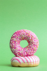 Two colourful donuts lies on green background. Vertical photography. Copy space for your text. Theme of delivery from Fast Food Restaurant