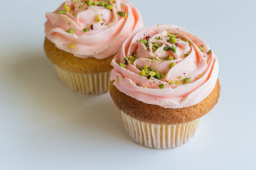 Pink cupcakes on white background - frosted cup cakes decorated with green pistachio sprinkles - with selective focus