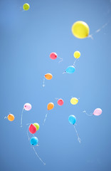 A lot of colorful balloons flying up against a bright blue sky