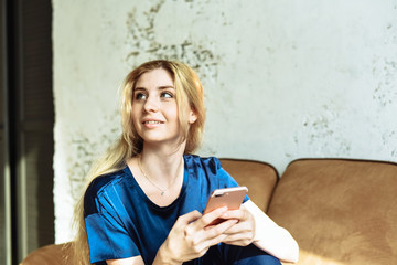 A young woman surfs the internet on the phone and smiles and laughs. Browse social networks at home while sitting on the couch