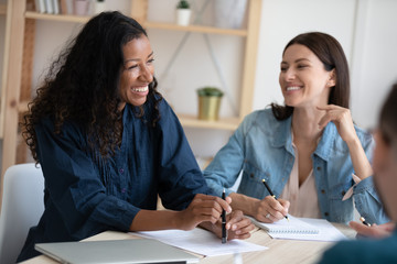 Smiling african american businesswoman telling employees about project in coworking boardroom during meeting break. Laughing diverse female leader discuss business strategy colleagues.