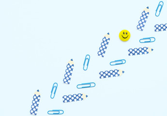 Face shaped yellow magnet, blue clips, pencil shaped paper stickers on white background. School and office supplies, stationary. Back to school concept. Flat lay style with copy space.