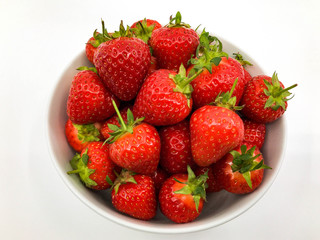 Plump ripe fresh strawberries in a white bowl on a plain white background.