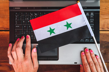 woman hands and flag of Syria on computer, laptop keyboard
