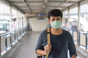 Asian man wear surgical face mask for protect coronavirus,covid19, carrying shoulder bag walking on the skywalk after traveling by skytrain in Bangkok, Thailand