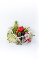 Fresh vegetables in a string bag on a white background. cabbage, zucchini, eggplant, carrots, lettuce, graffiti, bell pepper green, red. top view, place for text on top. no plastic.