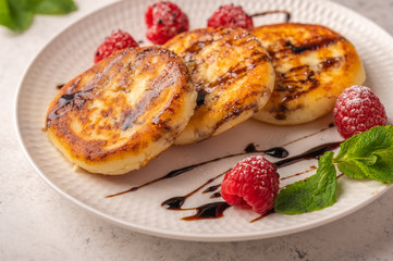 Homemade cheesecakes with raspberries, syrup and mint on a ceramic plate on a light wooden background. Close up. Copy space for text