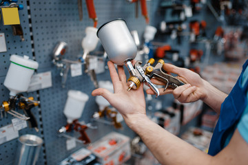 Male worker holds pneumatic paint gun, tool store