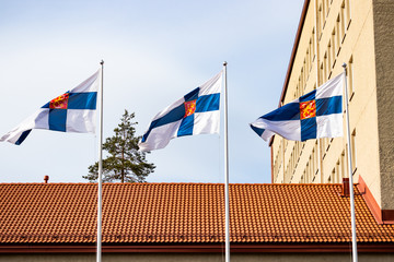 Three finnish national flags with coat of arms on the wind against the blue sky