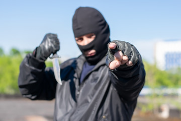 a bandit in a black mask, balaclava, points a finger and threatens to kill with a knife in the street