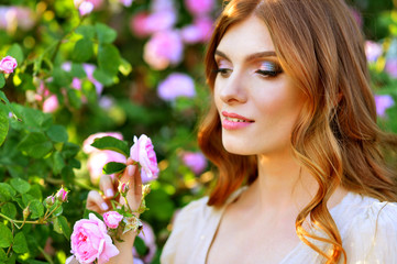 Naklejka premium Portrait of beautiful young woman posing by rose bush in summer park
