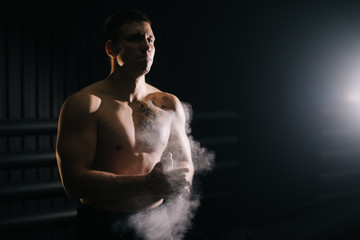 Weightlifter clapping hands with talc before lifting barbell at the gym. Strong muscular male preparing for fit workout in gym with chalk magnesium carbonate.