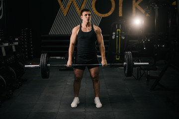 Obraz na płótnie Canvas Muscular athletic man with perfect beautiful body wearing sportswear holding heavy barbell during sport workout training in modern dark gym. Concept of healthy lifestyle.