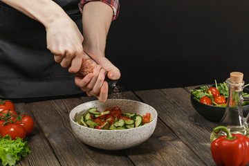 Woman salting fresh healthy vegetable salad on wooden table. Female hands with copyspace.