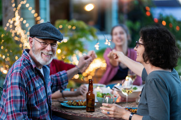 In the evening, dinner with the family around a table in the garden, in front of the wooden house. Everybody is having fun lighting spark sticks.