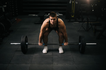 Fototapeta na wymiar Young strong man with perfect beautiful body wearing sportswear lifting heavy barbell from floor during sport workout training in modern dark gym. Concept of healthy lifestyle.