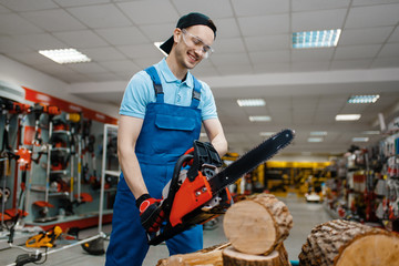 Worker in uniform testing chainsaw in tool store