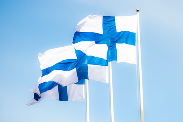 Fototapeta premium Three finnish national flags on the wind against the blue sky