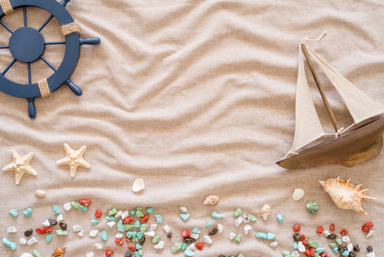 Summertime concept with straw hat, rudder, decorative yacht, seashells and starfishes on fabric background imitating sand with copy space.