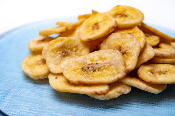 Healthy snack, crispy dehydrated unsugared banana chips on recycled glass plate on white background