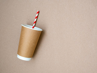 Takeaway coffee mug with paper white and red drinking straw on craft paper background. The concept of a world without plastic and a clean planet. Space for text. Zero waste. Flat lay, top view