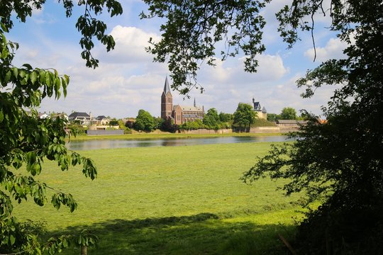 View from Beesel over green agriculture field and river Maas with boat on medieval church and castle of Kessel