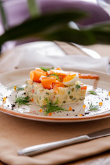 Traditional Russian salad Olivier. Salad is decorated with salmon and quail egg. Against the background of a wooden served table
