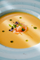 cream of salmon soup, in a bright blue plate, decorated with pieces of salmon, microgreens and butter. On the background of a wooden table.