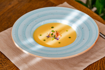 cream of salmon soup, in a bright blue plate, decorated with pieces of salmon, microgreens and...