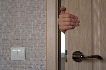 Hand of the woman who is behind the door, hold the door, opening or closing it. Concept: Disturbance of peace, invasion of privacy.