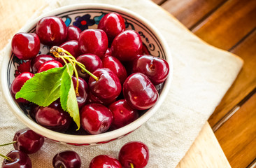 Beautiful bright red berries of sweet cherry. Close-up. Juicy sweet cherry berries in ceramic bowl on brown wooden table. Linen cloth. Vegetarianism, raw food concept. Fruit vitamin background.