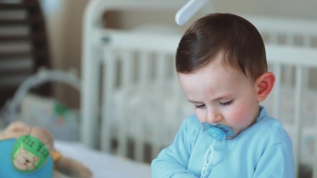 Close up of nice caucasian newborn baby on the bed and sucking a pacifier