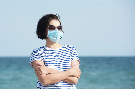Young woman in a mask standing on empty coast, protective equipment during coronavirus covid19. Social distance concept. - Powered by Adobe