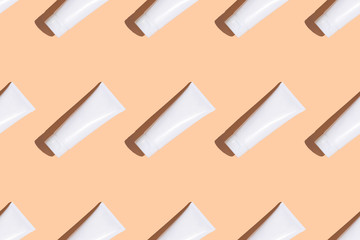 White cream tubes on lifht orange table. Care about face, hands, legs and body skin. Women beauty products. Cosmetic regular pattern. Empty place for logo on bottles. Hard light directly above flat