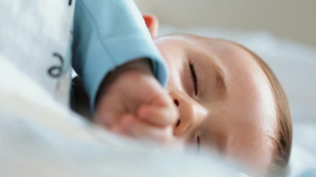 Close up of nice caucasian newborn baby on the bed and sucking a pacifier