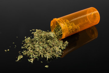 Close up of medical marijuana in yellow pill bottle on black background with mirror reflection