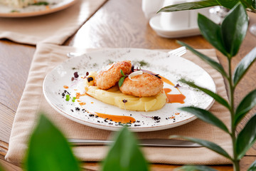 mashed potatoes with cutlet, on a beautiful white plate. The dish is decorated with micro-greens. Against the background of a wooden table in the interior.