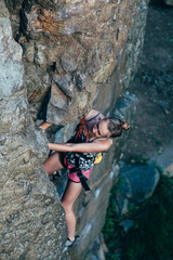 Young strong girl rock climber in a bright T-shirt climbing on a rock.