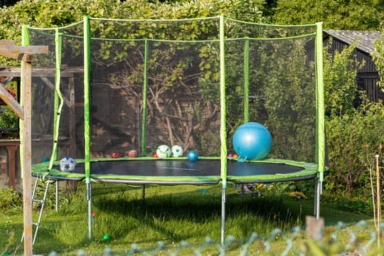 a fenced trampolin for children in a garden, there are some balls in it