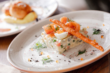 Traditional Russian salad Olivier. Salad is decorated with salmon and quail egg. Against the background of a wooden served table