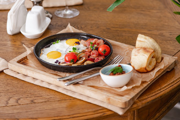 English breakfast. Fried eggs with fried sausages, bacon, tomatoes and mushrooms. On a wooden with bean paste.